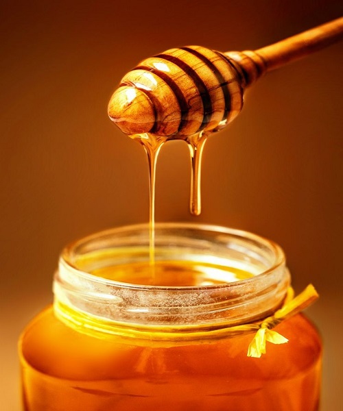 A glass jar of golden honey with a wooden dipper, showcasing its rich, natural texture and sweet appeal