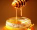 A glass jar of golden honey with a wooden dipper, showcasing its rich, natural texture and sweet appeal